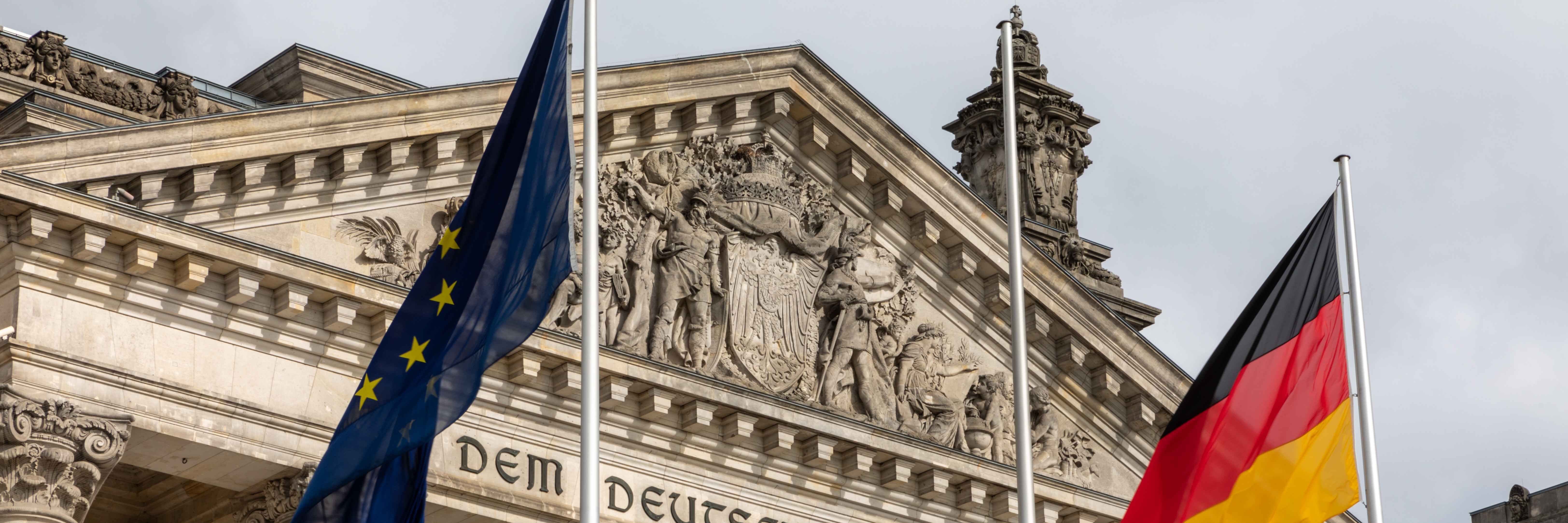 Berliner Reichstaggebäude mit Europa- und Deutschlandflagge im Vordergrung. (Ausschnitt)